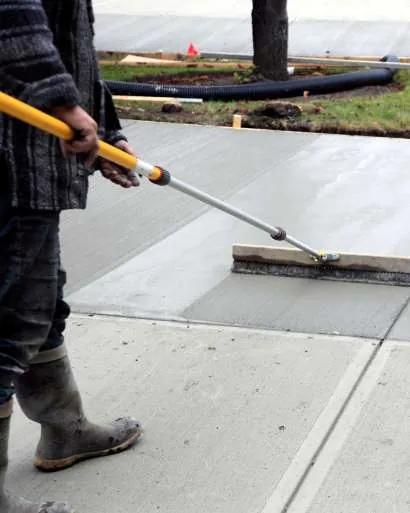 Fresh concrete slab being screeded beside a curb