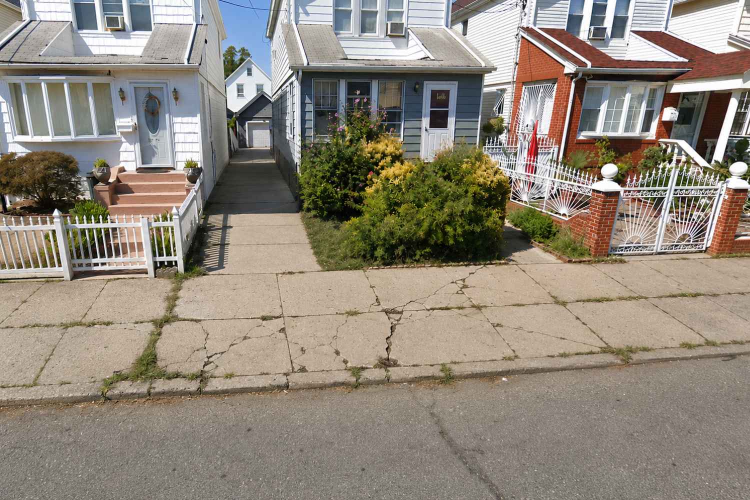 cracked and deteriorated sidewalk slabs with weed growth before repair in Jamaica Hills