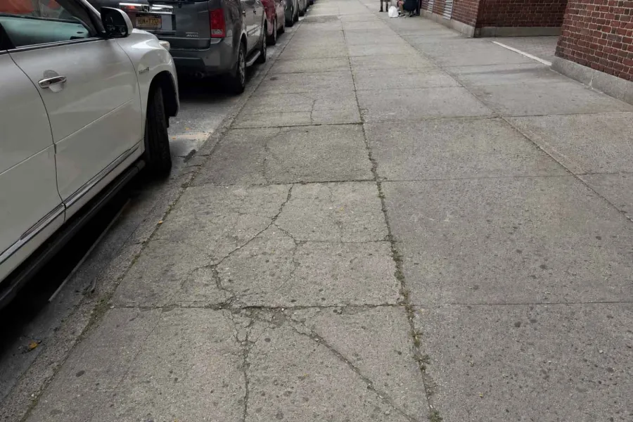 Cracked sidewalk before repair outside a Sunnyside rental building