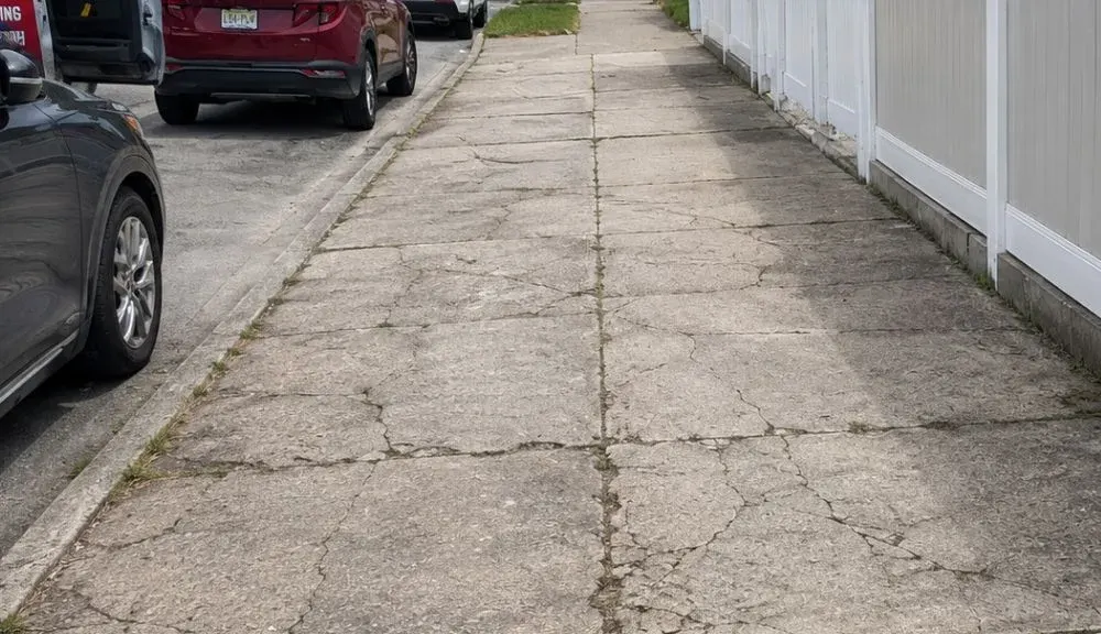 Cracked sidewalk slabs before repair at a Queens property